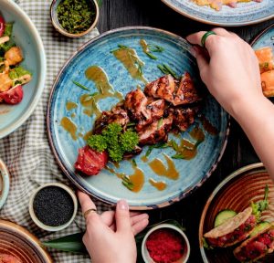 top-view-female-hands-putting-plate-with-roasted-chicken-with-grilled-tomato-fresh-herbs-sauce-table_141793-8510